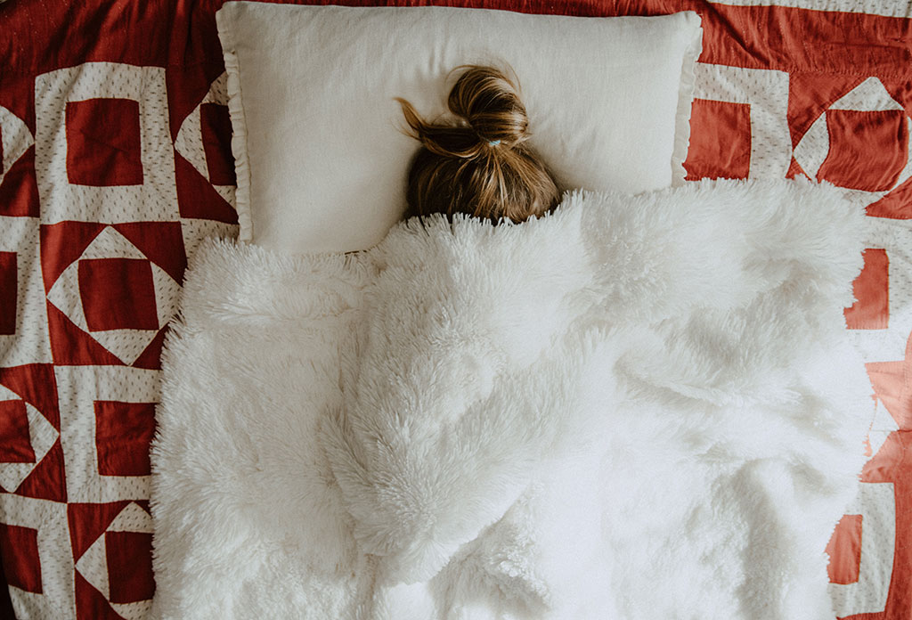 Woman hiding under a blanket with only her hair sticking out