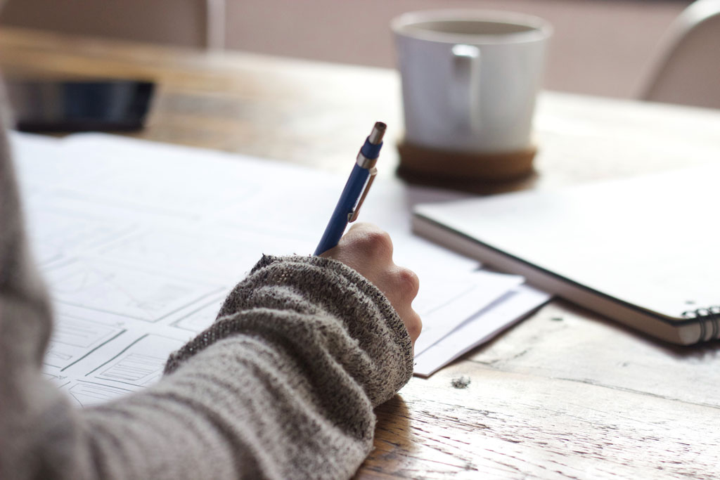 Desk covered with papers and notebook, person writing something