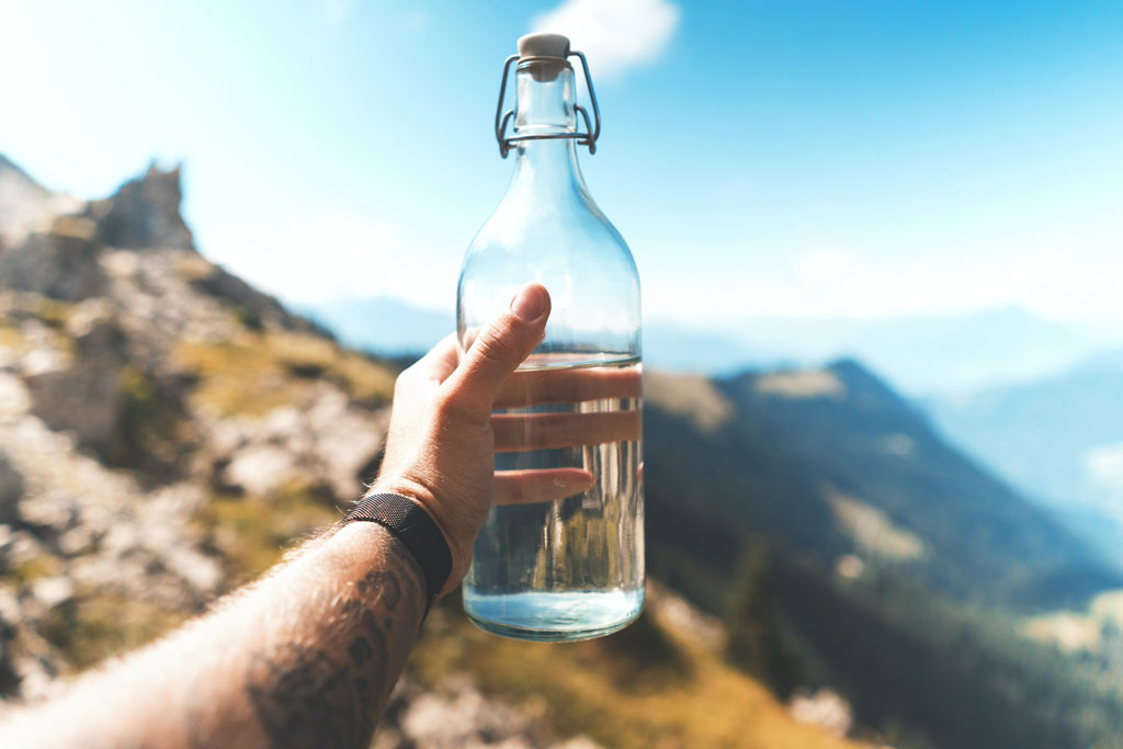 Person holding up a bottle of water in front of mountainous background