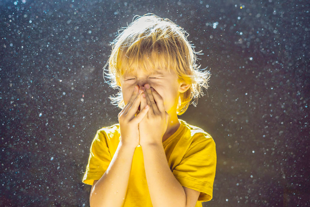 Child surrounded by dust particles holding eyes and nose closed