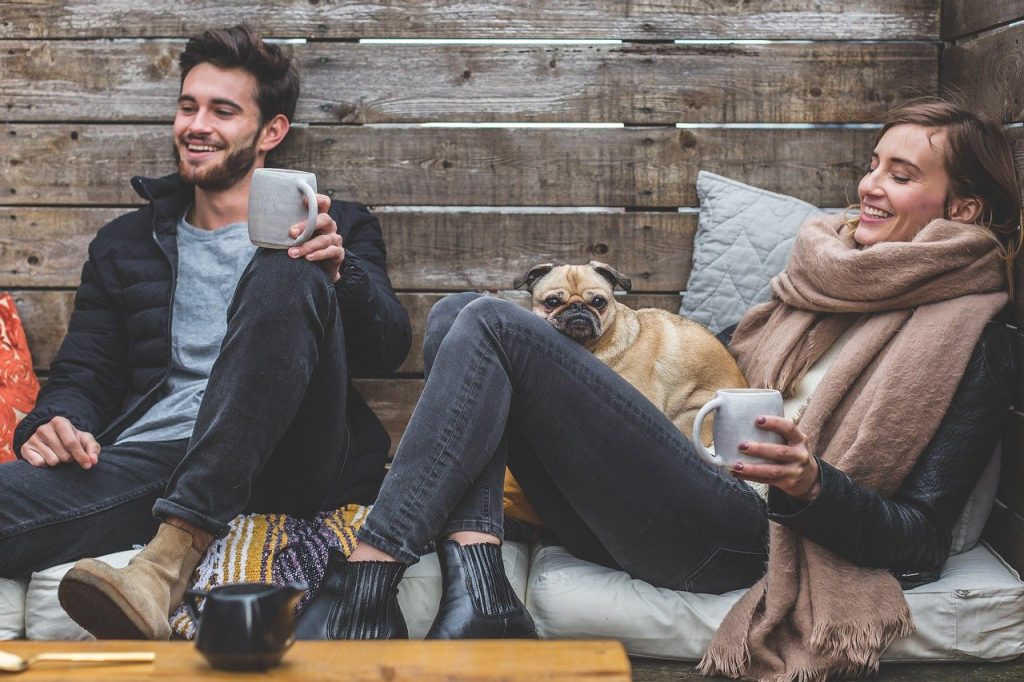 A happy couple with their dog sitting outside and drinking coffee