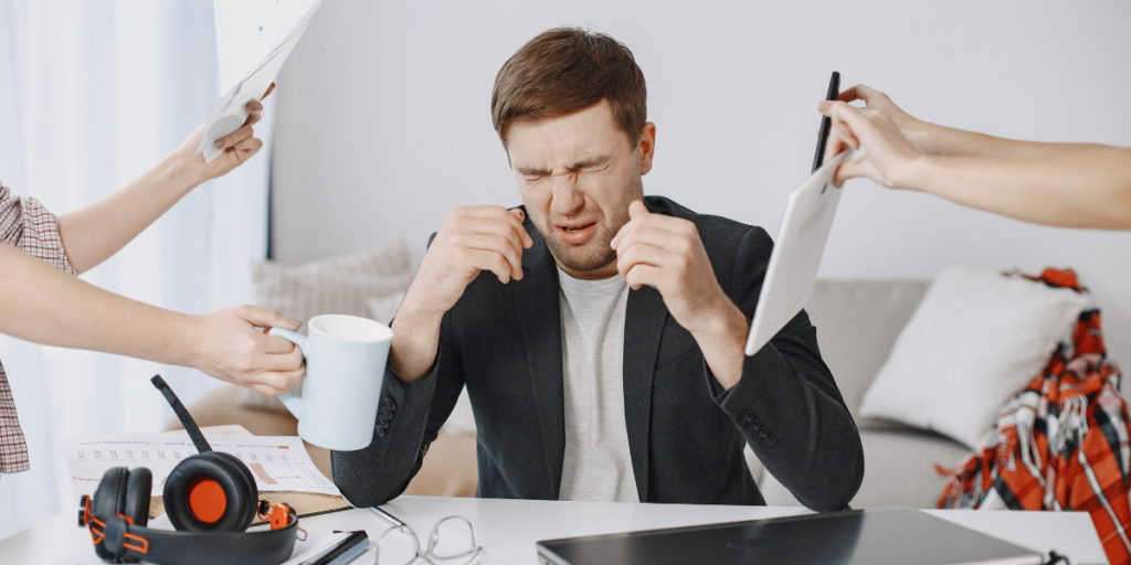 A man is sitting at an office desk and is feeling distress as he has a lot of work to do.